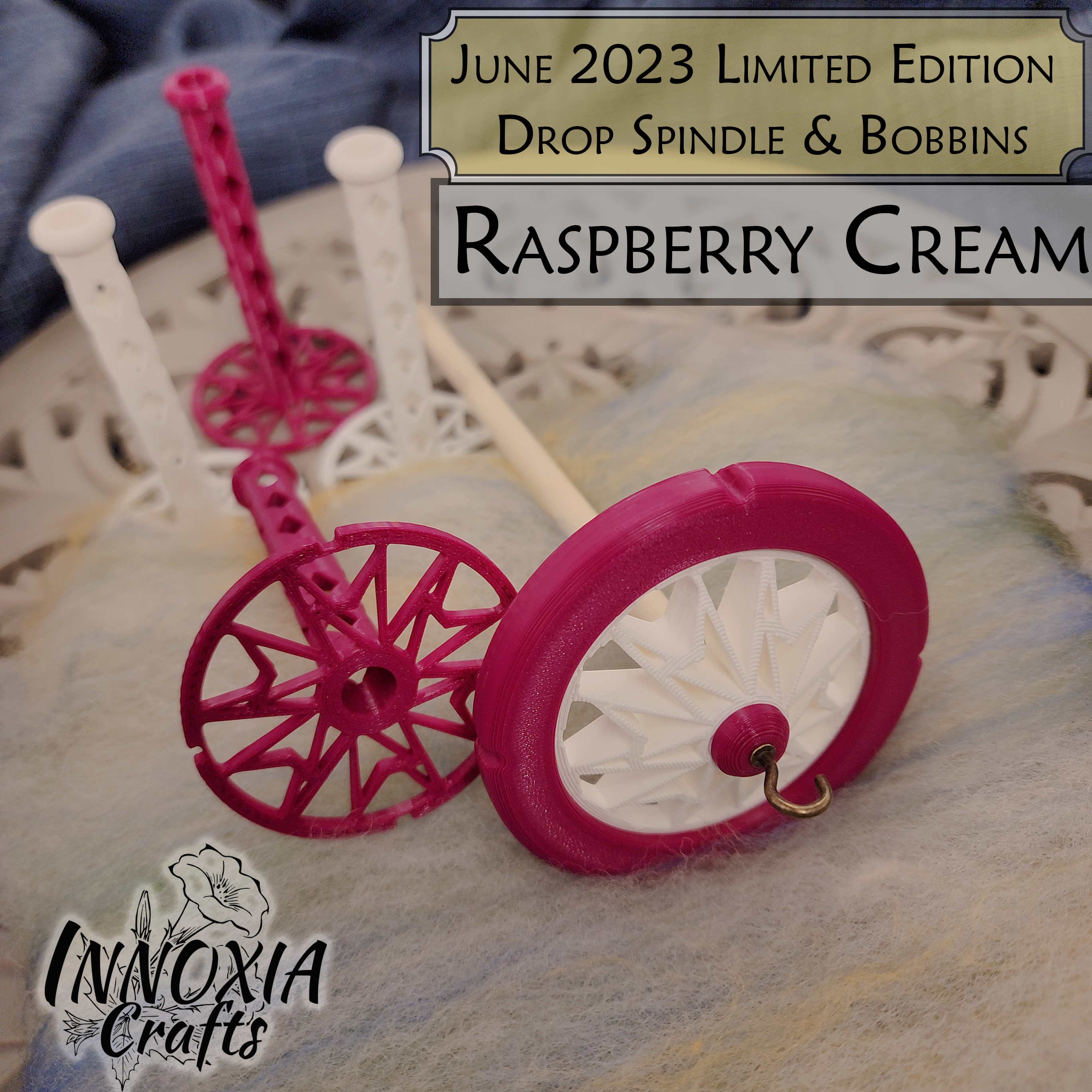 June 2023 Innoxia Crafts promotional image, showing a pink and white 3D-printed top-whorl spindle with a wood shaft and brass hook. Also shown are 4 matching bobbins, 2 pink and 2 white. The bobbins have only one flange (the big circular disk on the end of the shaft that stops thread coming off).